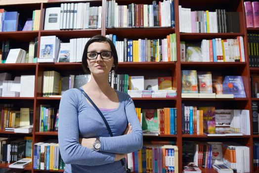 Pretty female student standing at bookshelf in university library store shop  searching for a book