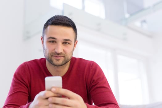 Handsome casual young man using a mobile phone at  home