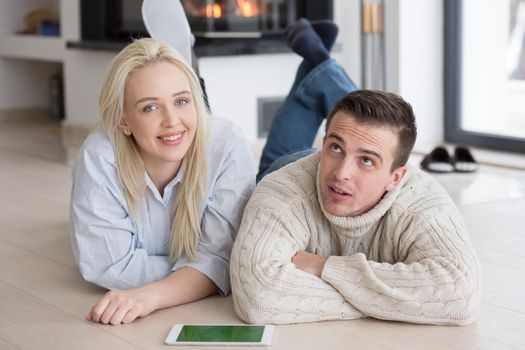 Young Couple on the floor in front of fireplace surfing internet using digital tablet on cold winter day