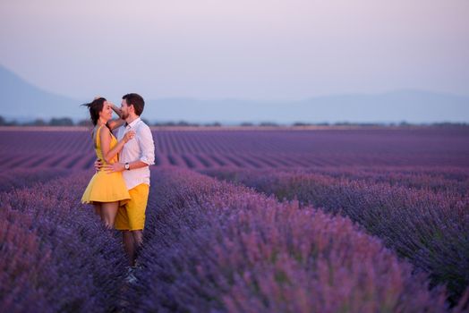 young loving couple having romantic time hugging and kissing on purple lavender flower field in sunset