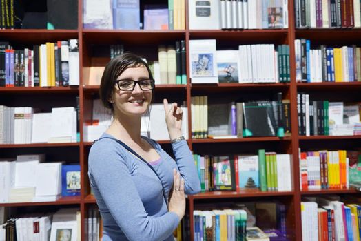 Pretty female student standing at bookshelf in university library store shop  searching for a book