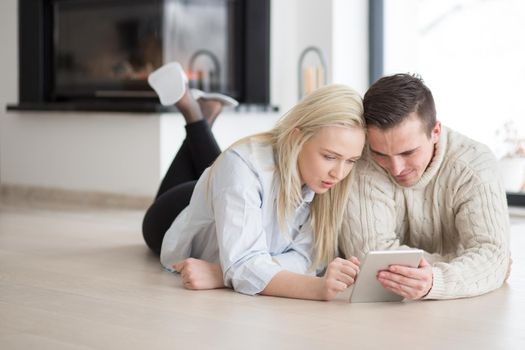 Young Couple on the floor in front of fireplace surfing internet using digital tablet on cold winter day