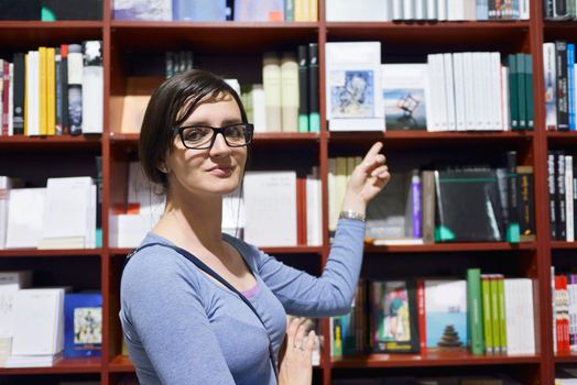 Pretty female student standing at bookshelf in university library store shop  searching for a book