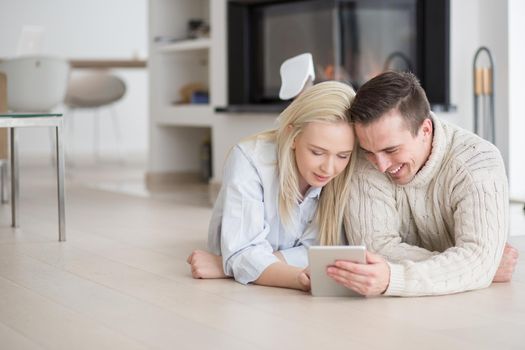 Young Couple on the floor in front of fireplace surfing internet using digital tablet on cold winter day