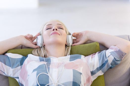 Young beautiful girl enjoying music through headphones, laying on sofa at home