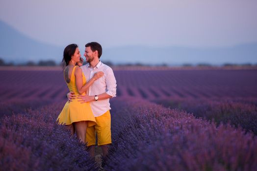 young loving couple having romantic time hugging and kissing on purple lavender flower field in sunset