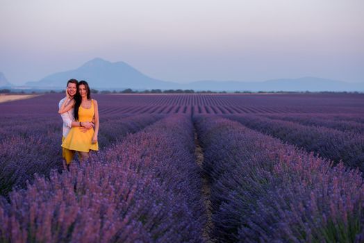 young loving couple having romantic time hugging and kissing on purple lavender flower field in sunset