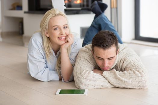 Young Couple on the floor in front of fireplace surfing internet using digital tablet on cold winter day