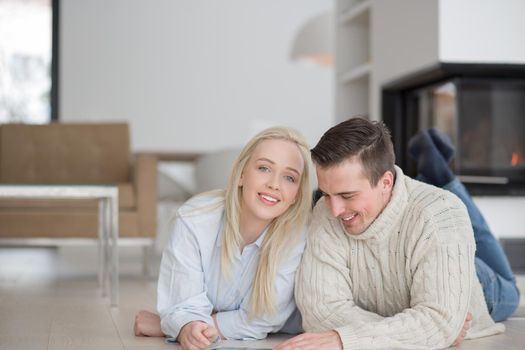 Young Couple on the floor in front of fireplace surfing internet using digital tablet on cold winter day