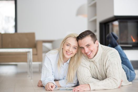 Young Couple on the floor in front of fireplace surfing internet using digital tablet on cold winter day