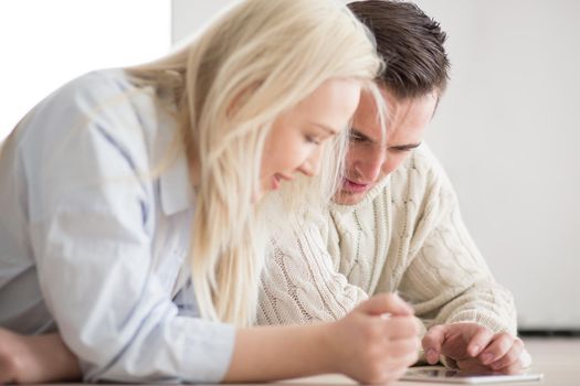 Young Couple on the floor in front of fireplace surfing internet using digital tablet on cold winter day