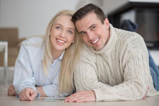 Young Couple on the floor in front of fireplace surfing internet using digital tablet on cold winter day