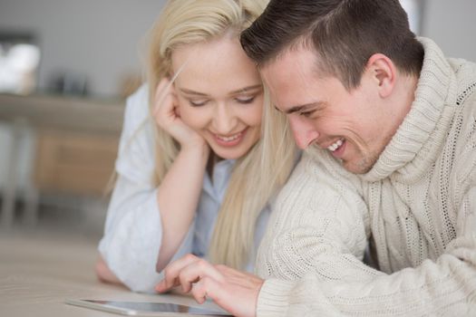 Young Couple on the floor in front of fireplace surfing internet using digital tablet on cold winter day