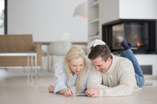 Young Couple on the floor in front of fireplace surfing internet using digital tablet on cold winter day