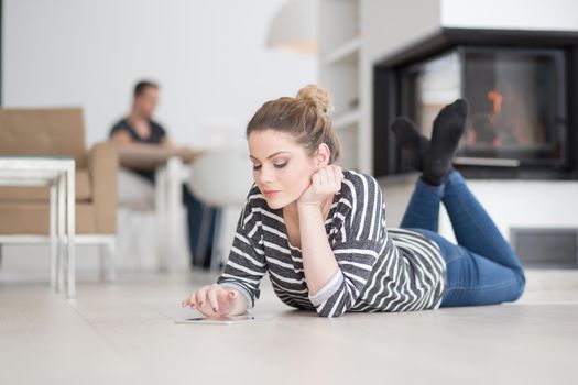 beautiful young woman websurfing using tablet computer on the floor in front of fireplace on cold winter day at home