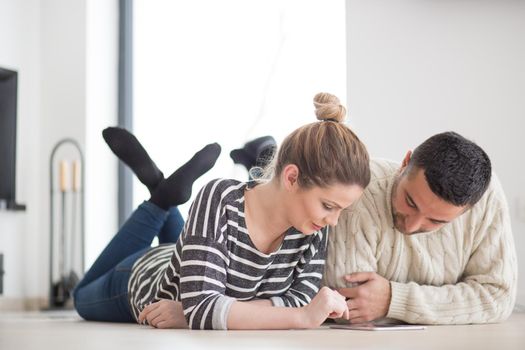 Young Couple on the floor in front of fireplace surfing internet using digital tablet on cold winter day