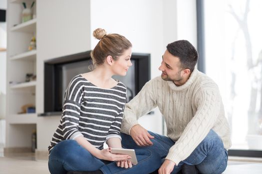 Young Couple on the floor in front of fireplace surfing internet using digital tablet on cold winter day