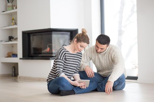 Young Couple on the floor in front of fireplace surfing internet using digital tablet on cold winter day