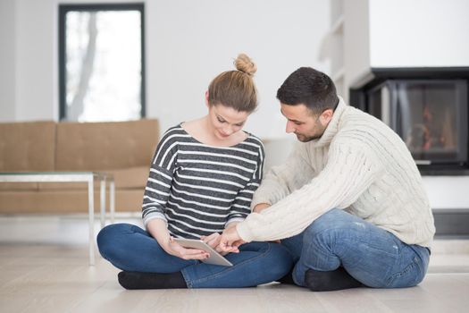 Young Couple on the floor in front of fireplace surfing internet using digital tablet on cold winter day