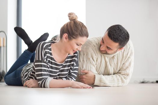 Young Couple on the floor in front of fireplace surfing internet using digital tablet on cold winter day