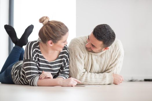 Young Couple on the floor in front of fireplace surfing internet using digital tablet on cold winter day