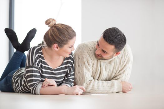 Young Couple on the floor in front of fireplace surfing internet using digital tablet on cold winter day