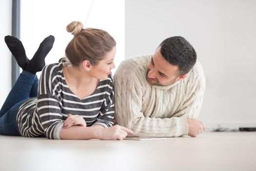 Young Couple on the floor in front of fireplace surfing internet using digital tablet on cold winter day