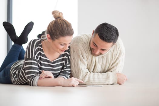 Young Couple on the floor in front of fireplace surfing internet using digital tablet on cold winter day