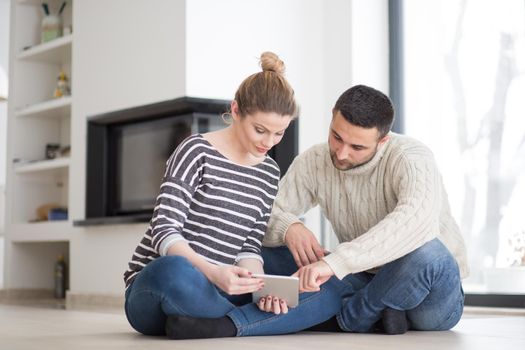 Young Couple on the floor in front of fireplace surfing internet using digital tablet on cold winter day