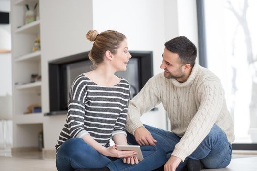 Young Couple on the floor in front of fireplace surfing internet using digital tablet on cold winter day