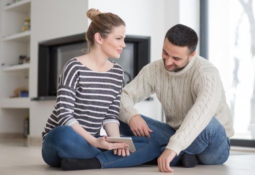 Young Couple on the floor in front of fireplace surfing internet using digital tablet on cold winter day