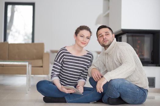 Young Couple on the floor in front of fireplace surfing internet using digital tablet on cold winter day