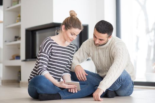 Young Couple on the floor in front of fireplace surfing internet using digital tablet on cold winter day