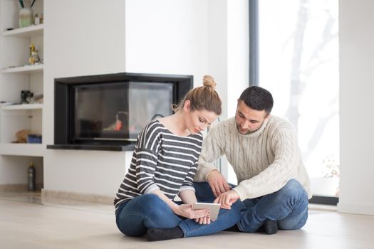 Young Couple on the floor in front of fireplace surfing internet using digital tablet on cold winter day