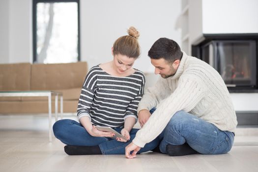 Young Couple on the floor in front of fireplace surfing internet using digital tablet on cold winter day