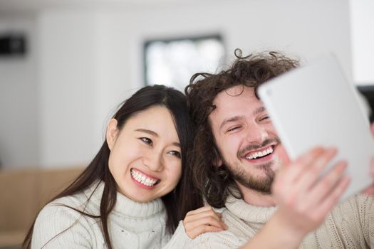 beautiful young multiethnic couple using tablet computer in front of fireplace on cold winter day at home