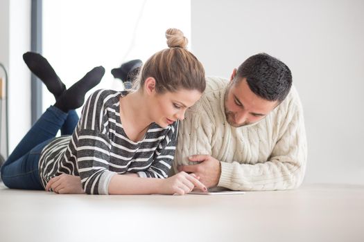 Young Couple on the floor in front of fireplace surfing internet using digital tablet on cold winter day