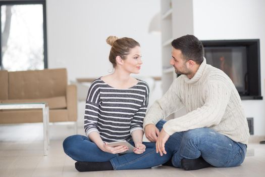 Young Couple on the floor in front of fireplace surfing internet using digital tablet on cold winter day