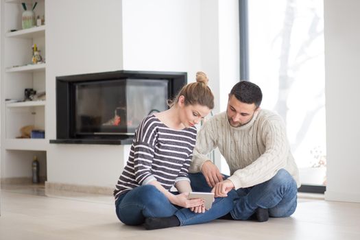 Young Couple on the floor in front of fireplace surfing internet using digital tablet on cold winter day