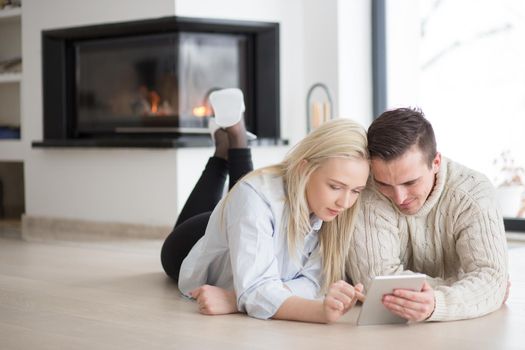 Young Couple on the floor in front of fireplace surfing internet using digital tablet on cold winter day