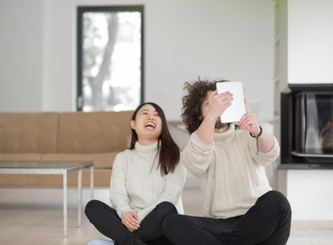 beautiful young multiethnic couple using tablet computer in front of fireplace on cold winter day at home