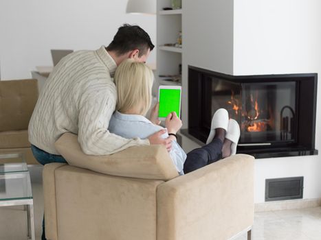 Young Couple in front of fireplace surfing internet using digital tablet on cold winter day at home