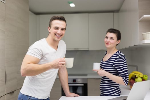 happy young couple with laptop computer enjoying morning coffee in modern kitchen at home