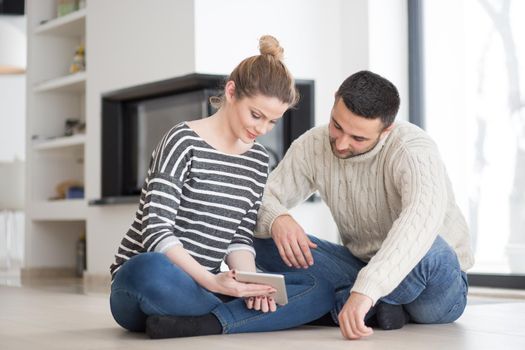 Young Couple on the floor in front of fireplace surfing internet using digital tablet on cold winter day