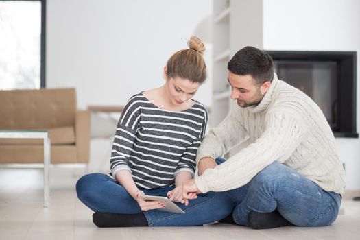 Young Couple on the floor in front of fireplace surfing internet using digital tablet on cold winter day