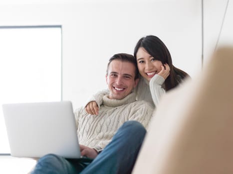 Young multiethnic couple relaxing at luxury home using laptop computer reading in the living room on the sofa couch.