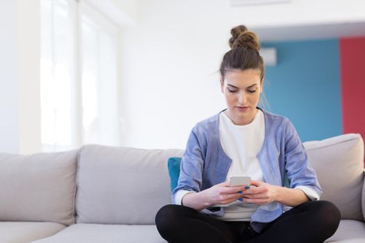 young happy woman using mobile phone on sofa at luxury home