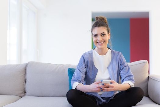 young happy woman using mobile phone on sofa at luxury home