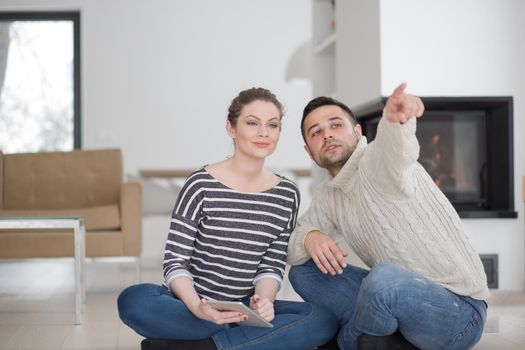 Young Couple on the floor in front of fireplace surfing internet using digital tablet on cold winter day