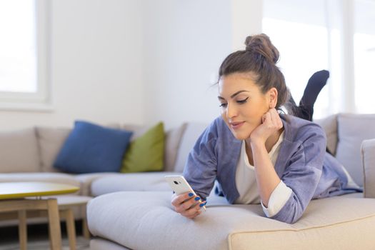 young happy woman using mobile phone on sofa at luxury home